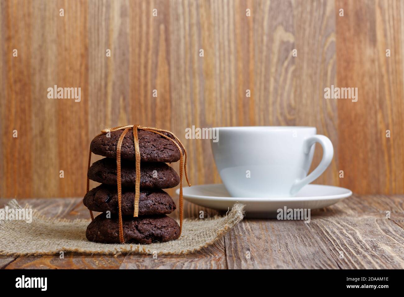 Stapel Schokoladenkekse und Tasse Kaffee auf Holztisch. Vorderansicht. Geringer Fokus. Stockfoto