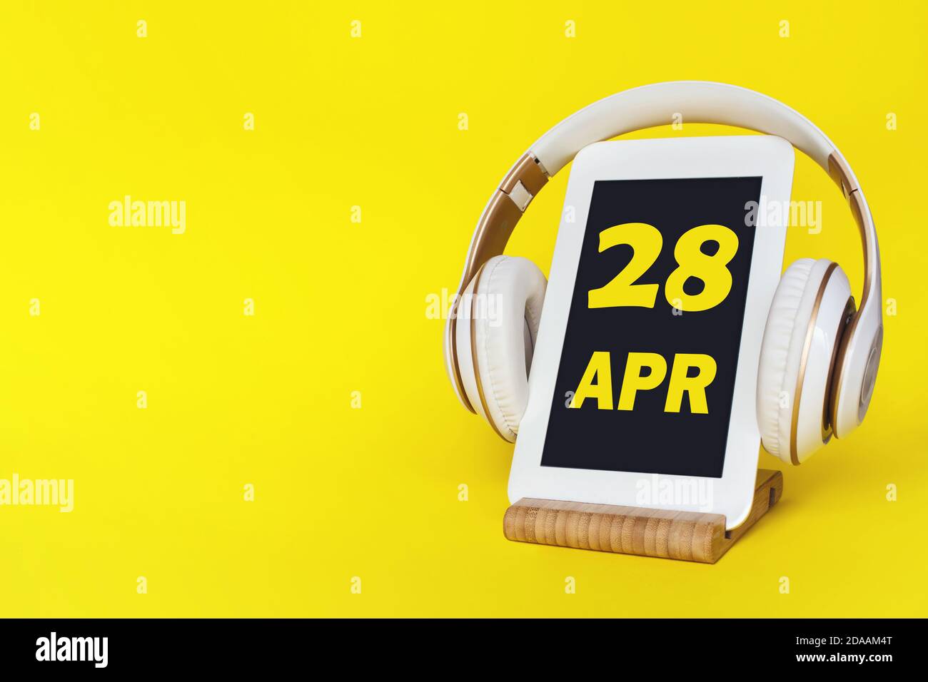 April. Tag 28 des Monats, Kalenderdatum. Elegante Kopfhörer und modernes Tablet auf gelbem Hintergrund. Leerzeichen für Text. Konzept Bildung, Technologie, Stockfoto