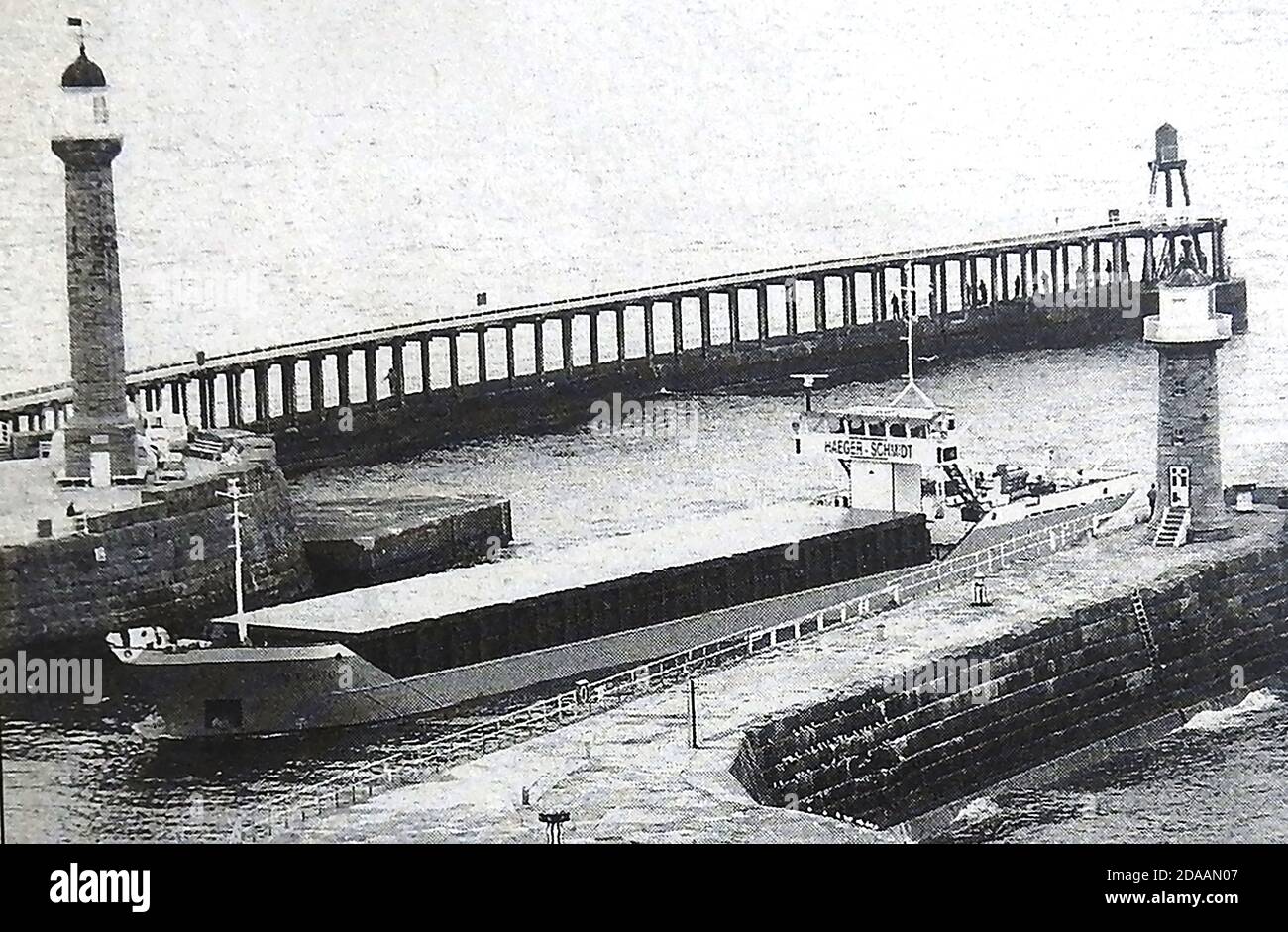 Ein historisches Foto der UNION PLUTO , eines der letzten Containerschiffe, die zwischen den viktorianischen Pfeilern und Leuchttürmen in Whitby, Yorkshire, Großbritannien, kurz vor dem Ende des Frachthandels vorbeifuhren. Das 82.5 Meter lange Frachtschiff Union Pluto wurde 1984 gebaut. (Rufzeichen MJAB). Stockfoto
