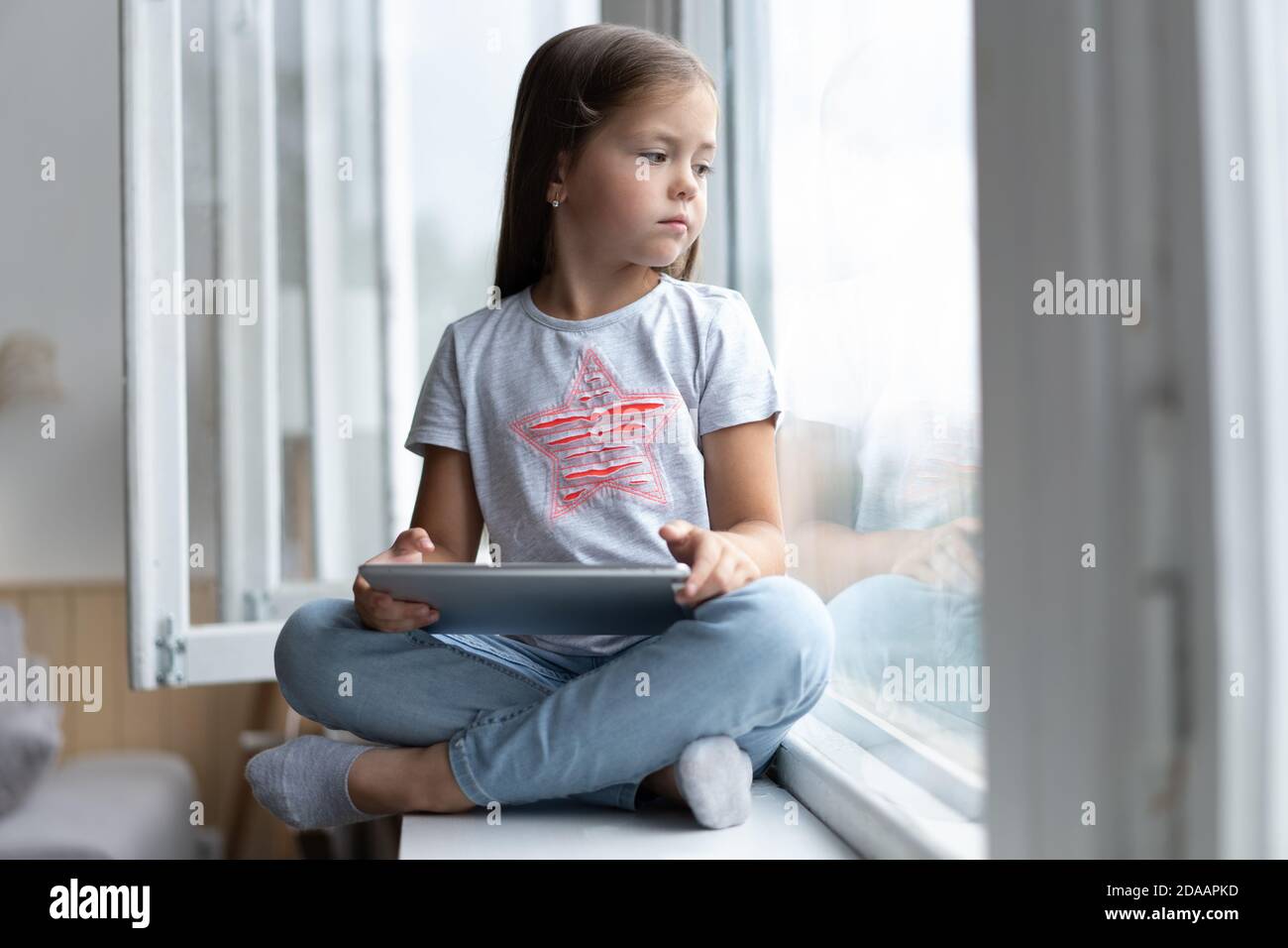 Nettes kleines Kind mit einem digitalen Tablet in einem Zuhause mit großem Fenster. Stockfoto
