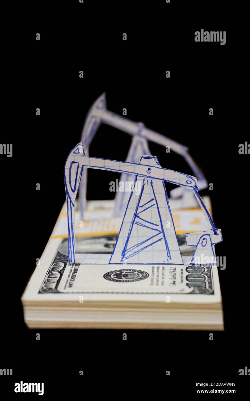 Petroleum-Kürbis und Ölbohrinseln aus Papier auf einer Packung von 100 Dollar Scheine. Geringer Fokus. Isoliert auf schwarzem Hintergrund. Stockfoto