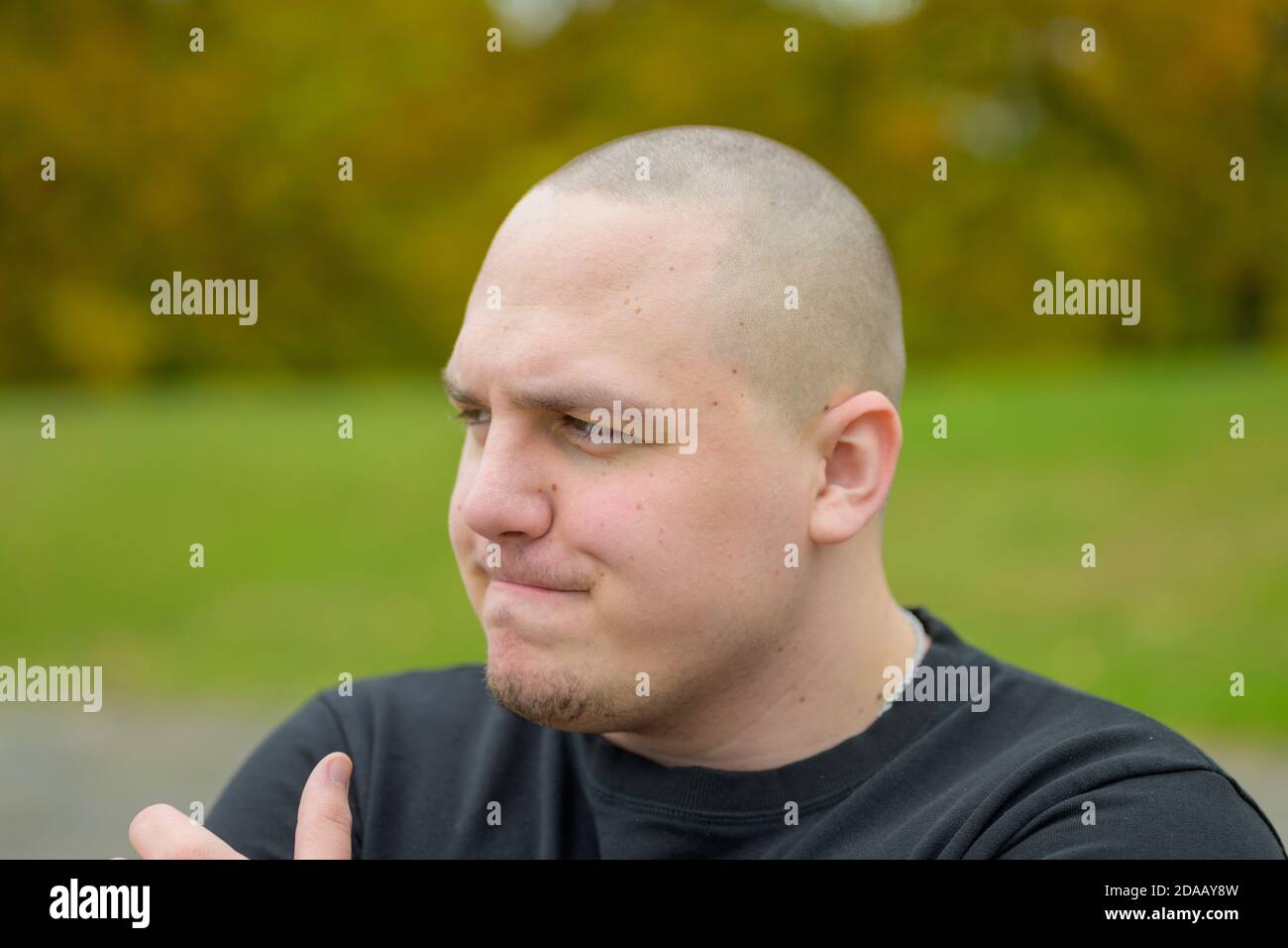 Nachdenklicher junger Mann, der mit seinem auf die Seite schaut Hand an sein Kinn und ein kontemplativer Ausdruck im Freien in Ein Garten oder Park Stockfoto