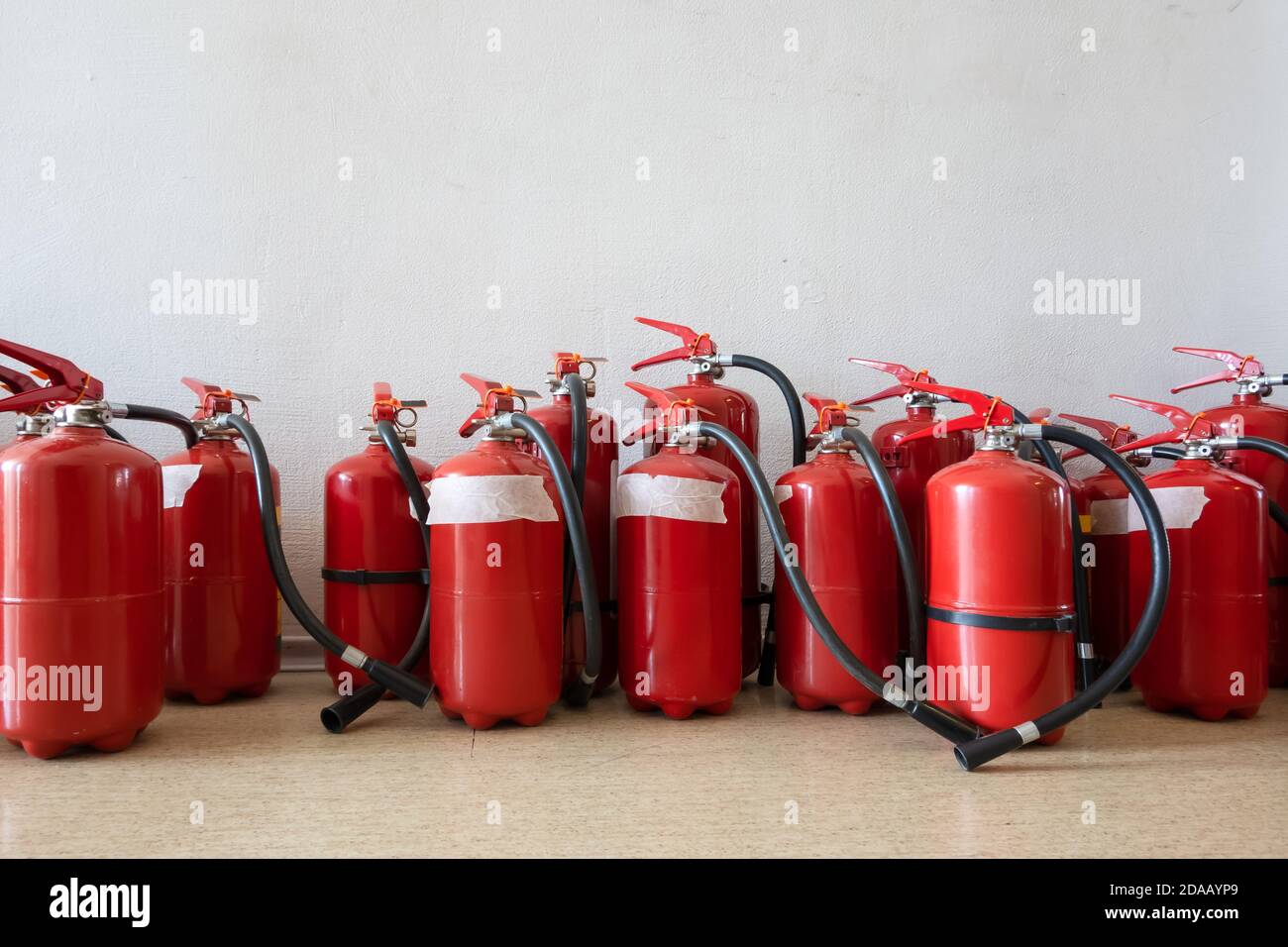 Ein Haufen abgelaufener Feuerlöscher auf dem Boden neben der Wand. Erneuerung der Feuerlöscher für Unternehmen. Stockfoto