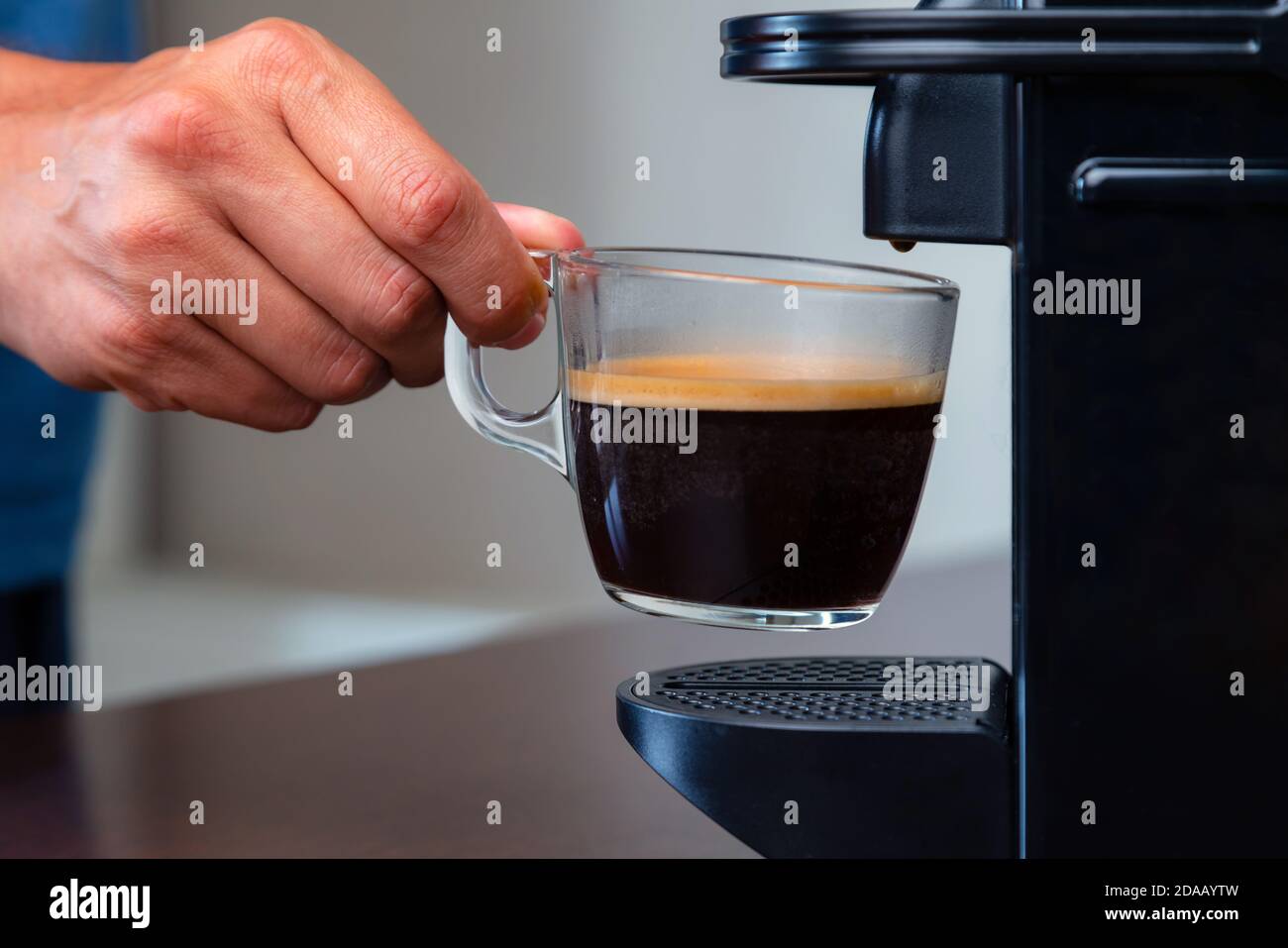 Nahaufnahme der Hand Abholung einer Tasse Espresso Kapsel Kaffeemaschine zu Hause. Konzept der Kaffeepause. Stockfoto