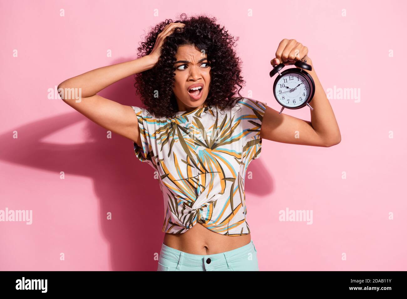 Portrait Foto von unsicher lockig afrikanische Frau zeigt Uhr Grimacing Missverständnis isoliert auf pastellrosa Farbe Hintergrund Stockfoto