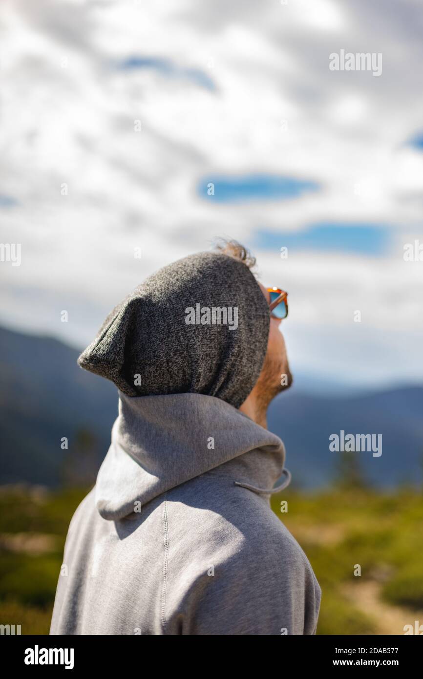 Junge weiße Mann von hinten mit Sonnenbrille in schönen natürlichen Umgeben von Bergen mit Blick auf den wolkigen Himmel Stockfoto