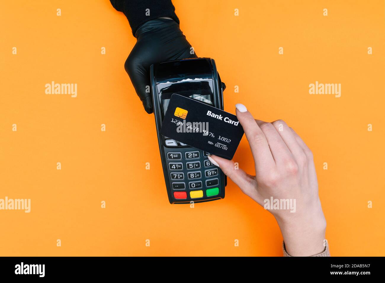 Verkäufer in schwarzen Einweghandschuhen hält ein Zahlungsterminal in der Hand. Der Käufer bezahlt den Kauf mit einer Bankkarte. Sicheres Einkaufen während der Stockfoto