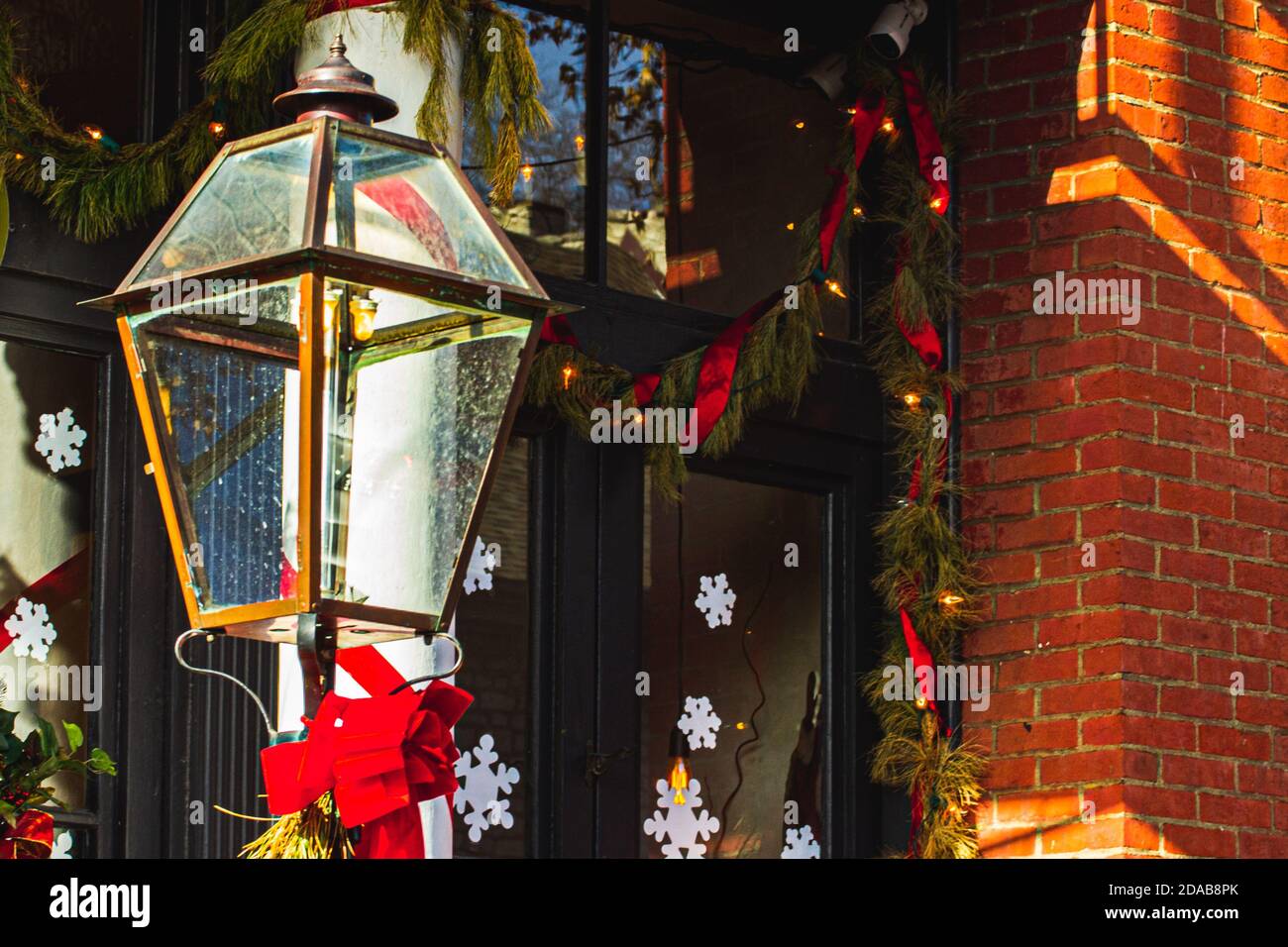 Messinglampen-Säule vor dem rustikalen Backsteingebäude Beide sind mit traditioneller Weihnachtsgirlande und roten Bändern dekoriert Stockfoto