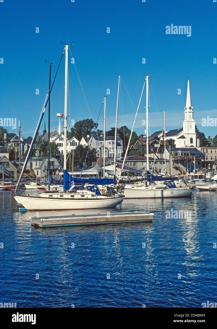 Der charmante Küstenhafen von Camden, Maine, USA, ist die ikonische Stadt New England mit seiner weißen Kirchtürmkirche und einem Hafen voller moderner und klassischer Segelboote. Dazu gehören historische Schoner, die Segeltörns in Penobscot Bay und entlang der nordöstlichen Küste am Atlantischen Ozean anbieten. Stockfoto
