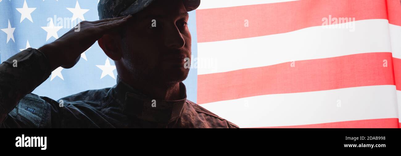 Patriotischer Militärmann in Uniform und Mütze, der neben der amerikanischen Flagge auf dem Hintergrund grüßt, Banner Stockfoto