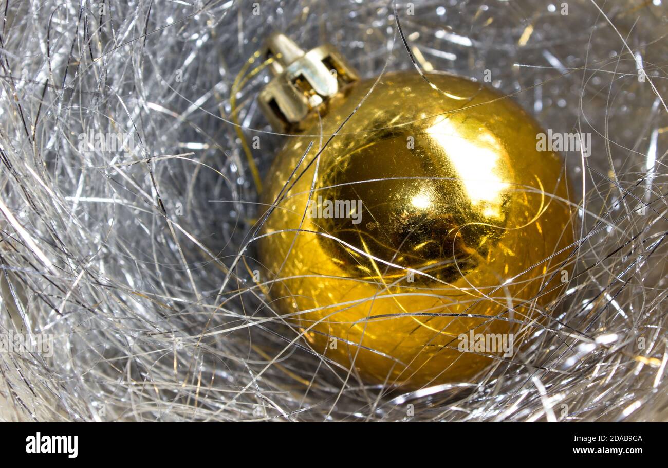 Ein goldener Weihnachtsball, umgeben von einem silberfarbenen Lametta Stockfoto