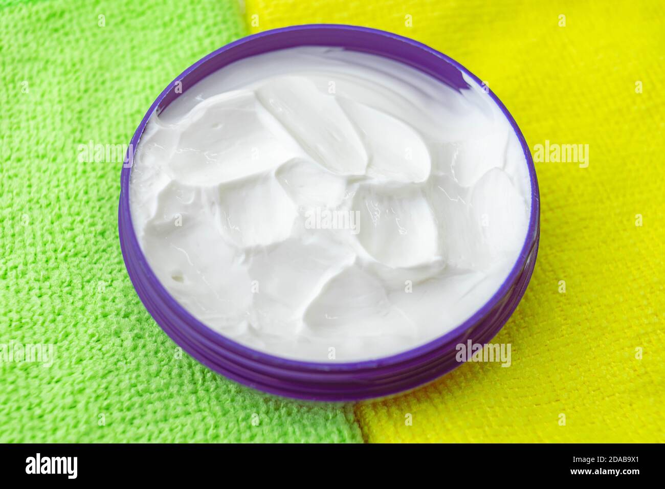 Dunkelblau offener runder Behälter mit weißer Creme auf grün gelben Handtüchern. Stockfoto