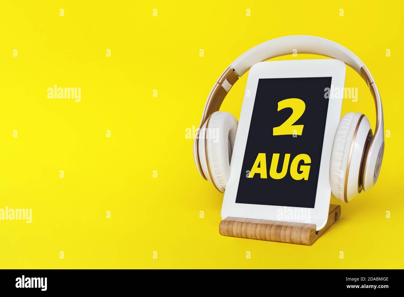 August. Tag 2 des Monats, Kalenderdatum. Elegante Kopfhörer und modernes Tablet auf gelbem Hintergrund. Leerzeichen für Text. Bildung, Technologie, Lifestyle Stockfoto