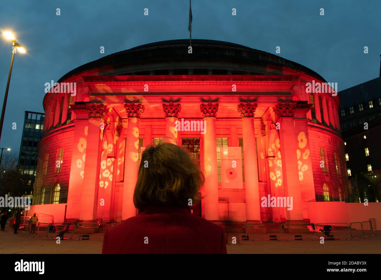 Waffenstillstandstag Gedenkfeier während der Aussperrung. Manchester Central Library, UK beleuchtet mit rotem Licht und Mohn-Design. Frau schaut auf. Öffentliches Gebäude. Stockfoto