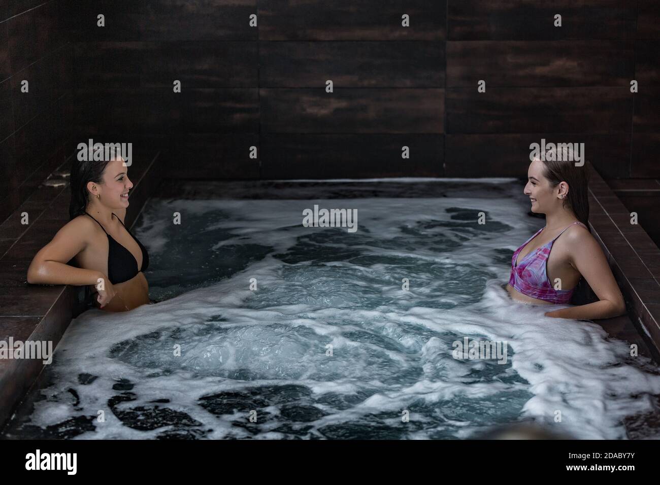 High Angle Seitenansicht der fröhlichen jungen Freundinnen chillen zusammen In sprudelndem Wasser und genießen Sie Hydromassage, während Sie Zeit verbringen Im Spa-Pool Stockfoto