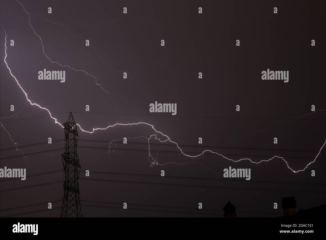 Ein gigantisches Gewitter blitzt durch einen Hochspannungsmast und Berührt die Dächer der umliegenden Häuser Stockfoto