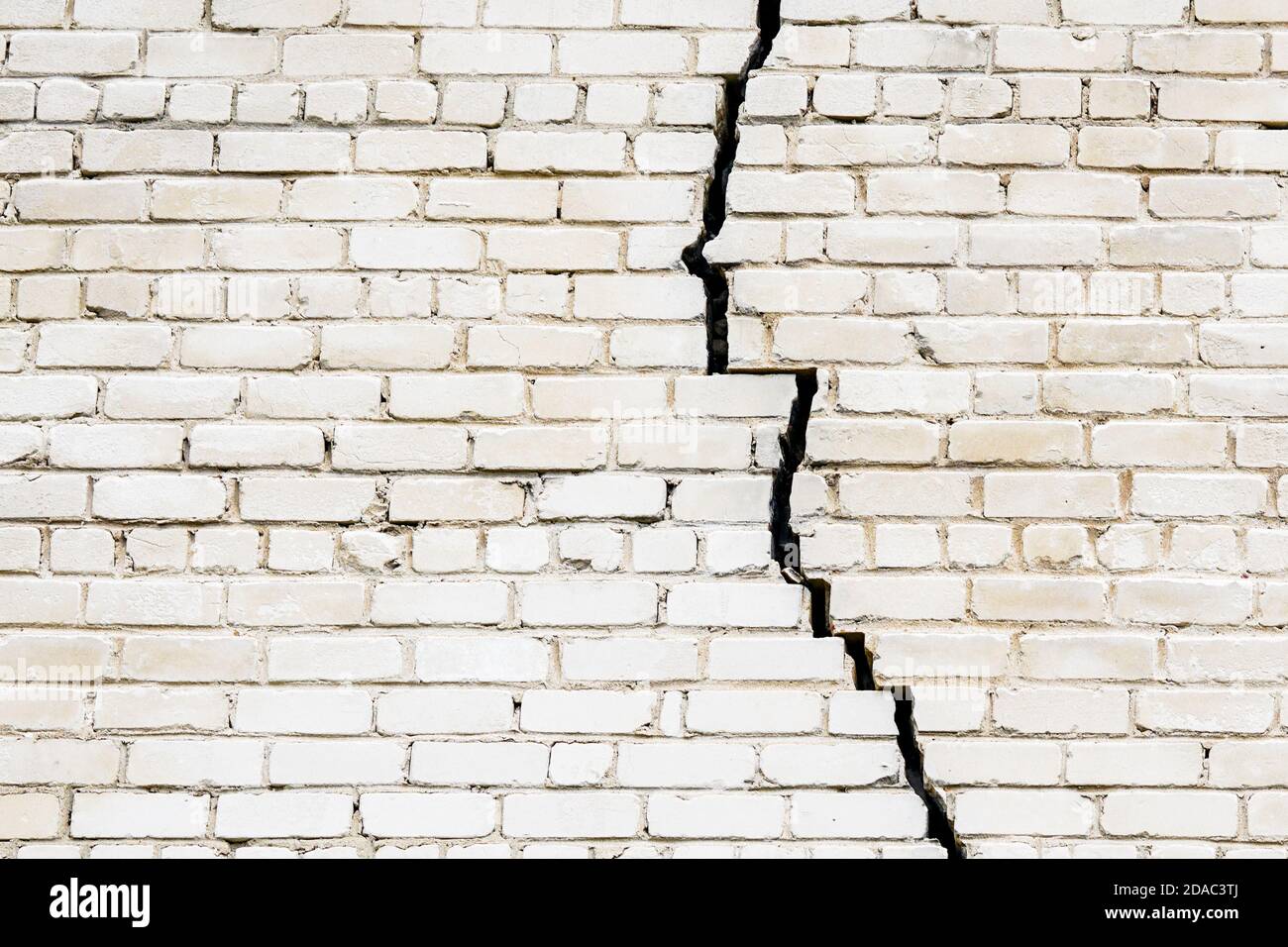 Ein großer langer und breiter Riss in einem weißen Ziegel Wand Stockfoto