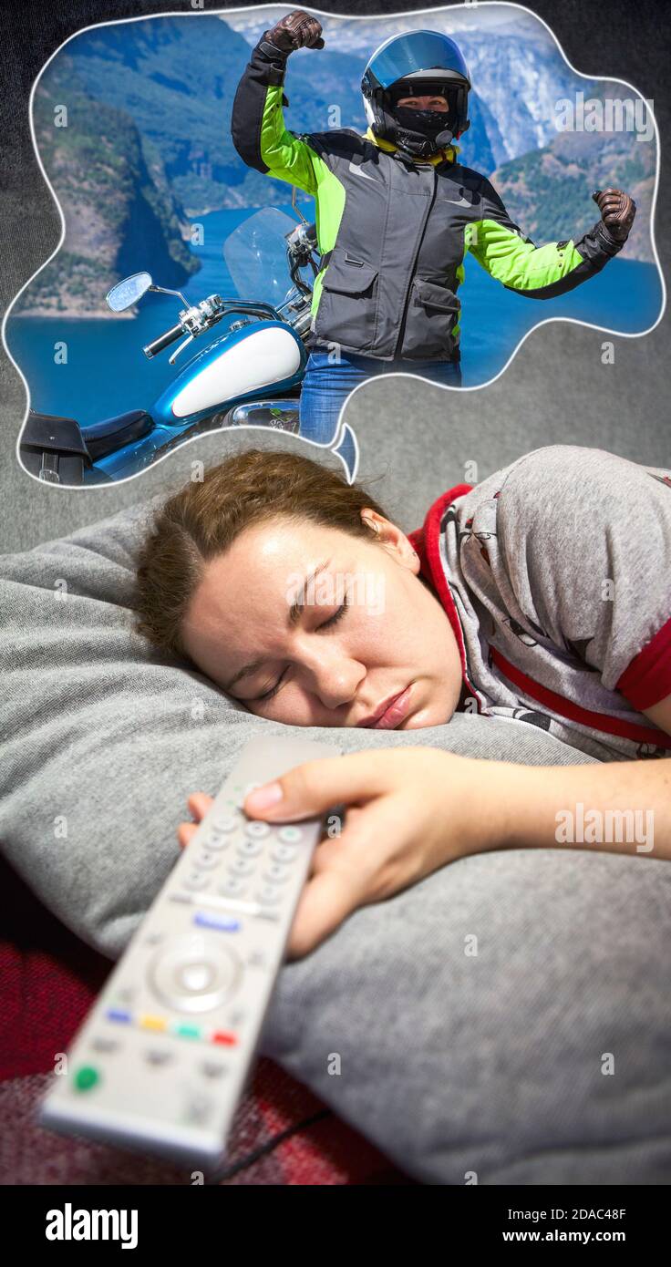 Junge kaukasische Frau schläft auf der Couch mit Tagträumen über Reisen mit dem Motorrad. Die Fernbedienung des Fernsehers ist in der Hand Stockfoto
