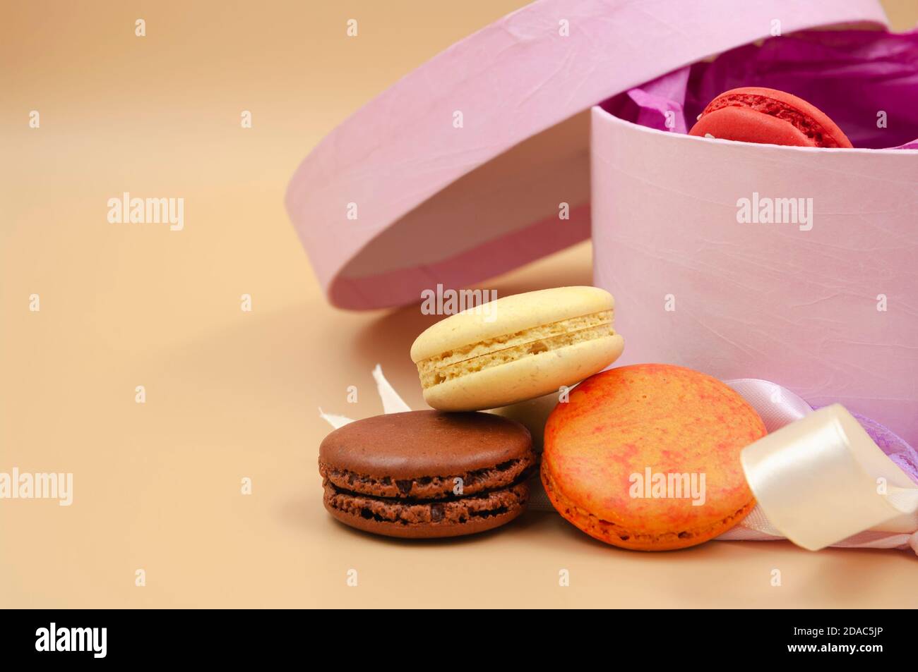 Vier farbenfrohe französische Macarons mit rosa Pappkarton auf pfirsichfarbenem Hintergrund. Stockfoto