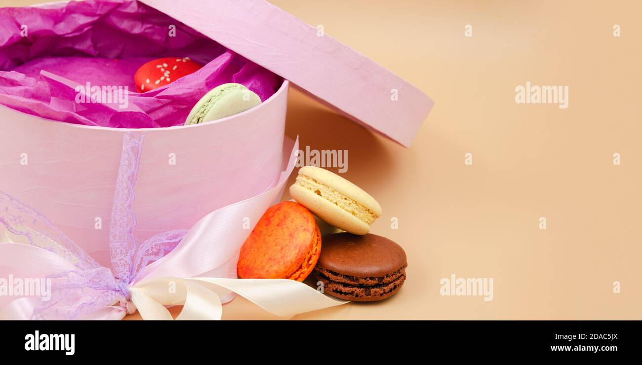 Vier farbenfrohe französische Macarons mit rosa Pappkarton auf pfirsichfarbenem Hintergrund. Stockfoto