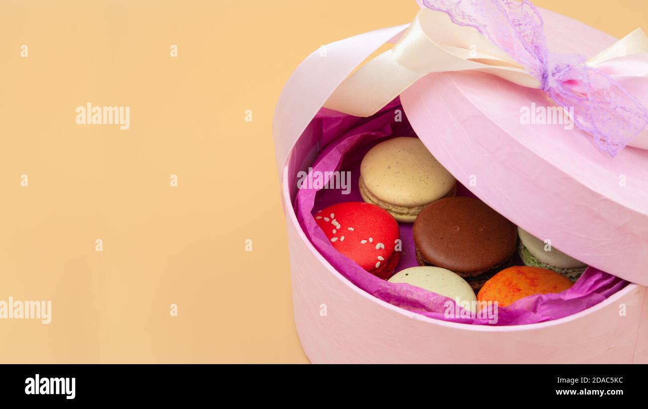 Vier farbenfrohe französische Macarons in rosa Pappkarton auf pfirsichfarbenem Hintergrund. Stockfoto