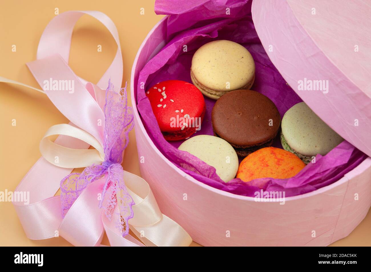 Vier bunte französische Macarons in rosa Karton auf Pfirsich Hintergrund Stockfoto