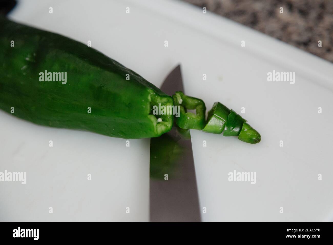 Grüner Paprika mit einem Messer in der Küche mit weißem Hintergrund geschnitten. Stockfoto