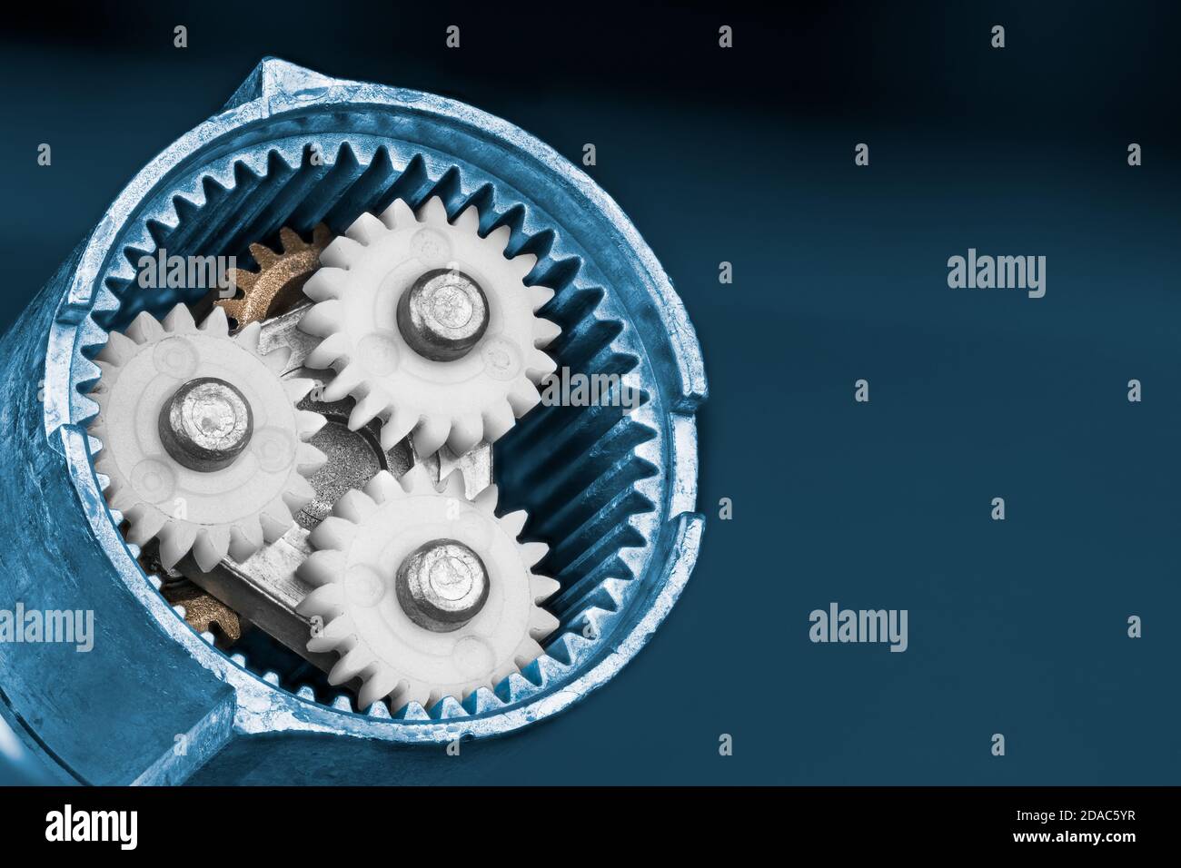 Weiße Planetenräder in einem Ringzahnrad epicyclischer Zahnradbahn auf blauem Hintergrund. Getriebe mit elektrischer Schraubpistole aus Kunststoff und Metall COG wheels.in. Stockfoto