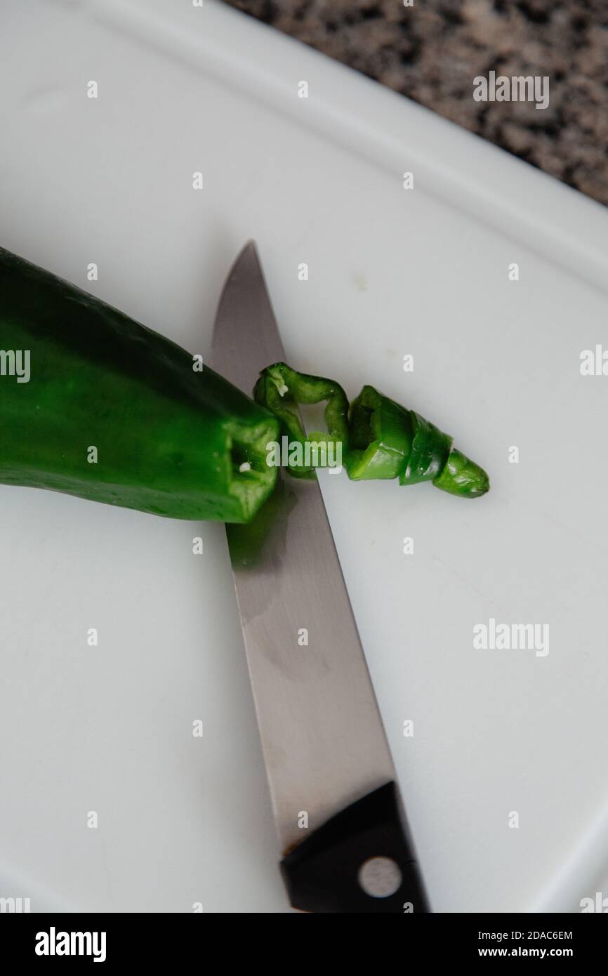 Grüner Paprika mit einem Messer in der Küche mit weißem Hintergrund geschnitten. Stockfoto