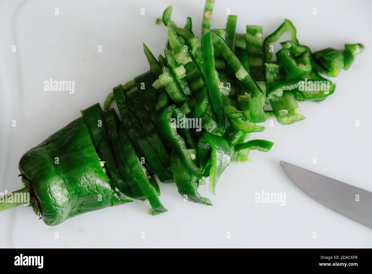 Grüner Paprika mit einem Messer in der Küche mit weißem Hintergrund geschnitten. Stockfoto