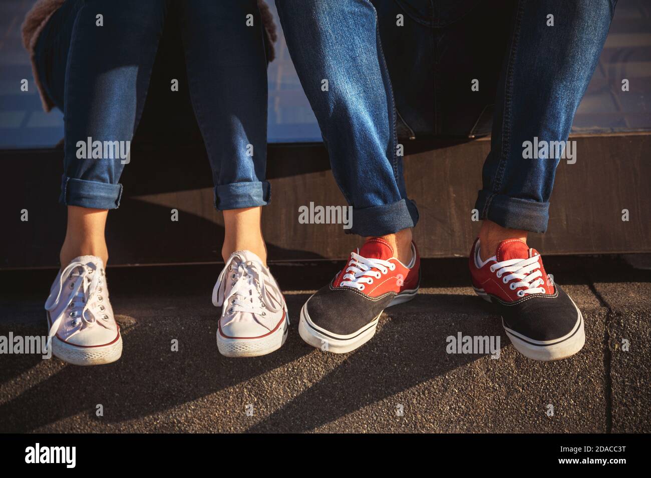 Oben Nahaufnahme von jungen Paar Beine in Turnschuhen und Jeans sitzen zusammen draußen. Stockfoto