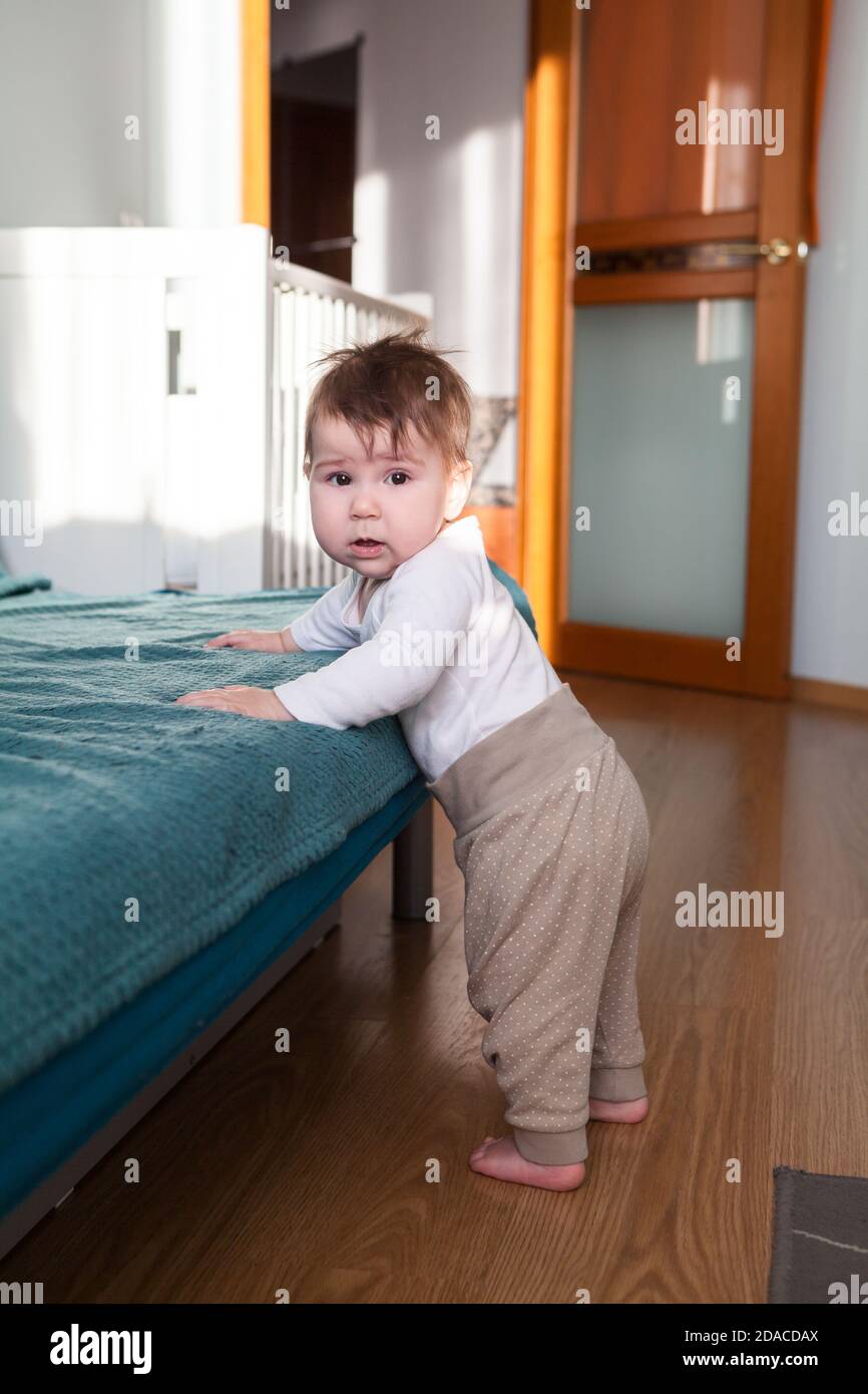 Kaukasischen Kleinkind Junge lehnt sich an Sofa dann versucht zu tun Erste Schritte in Apartment Zimmer Stockfoto