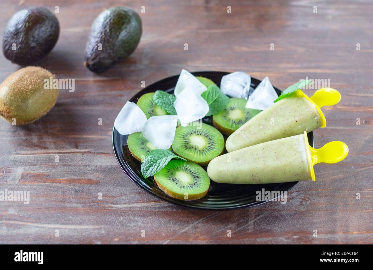 Hausgemachtes gesundes Sorbet (Fruchteis) aus Avocado und Kiwi auf dem schwarzen Teller unter Kiwi-Stücken, Minzblättern, Eiswürfeln auf dem alten Tisch Stockfoto