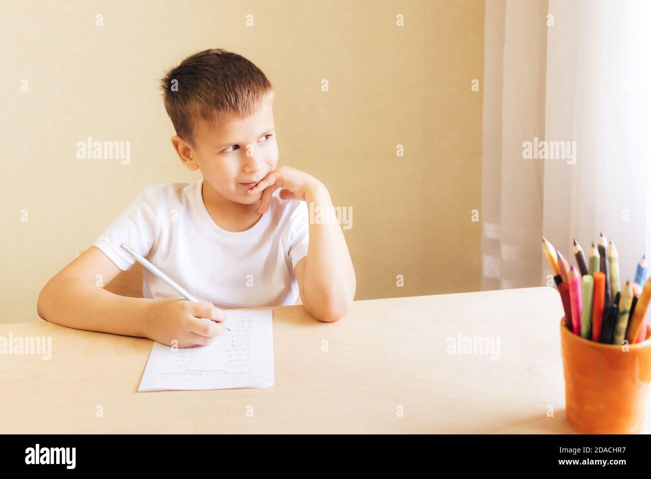 Nette kleine Schüler zu Hause lernen. 7 Jahre alter Junge macht Unterricht am Schreibtisch in seinem Zimmer. Stockfoto
