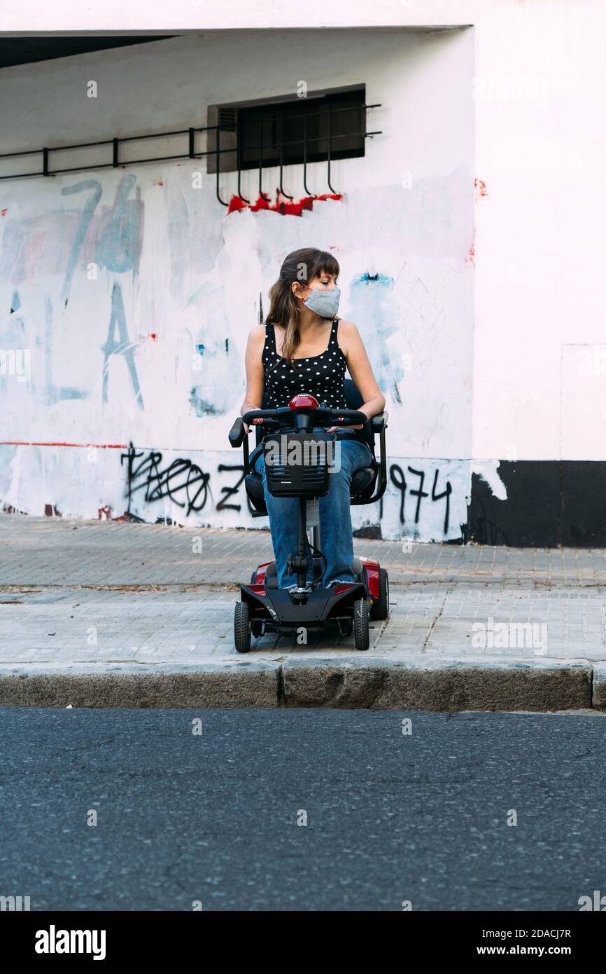 Junge Frau in Elektroroller für Behinderte. Sie kann die Straße nicht überqueren, weil es keine Rampe gibt. Grunge Wand im Hintergrund. Stockfoto