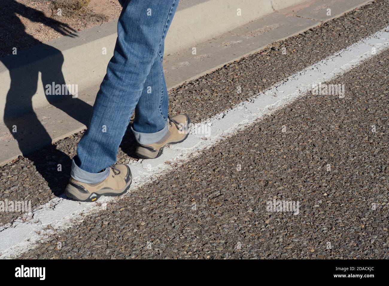 Eine Frau testet ihr Gleichgewicht, indem sie eine weiße Linie entlang des Straßenrandes entlang läuft, ähnlich einer Nüchternheit, die von der Polizei durchgeführt wird. Stockfoto
