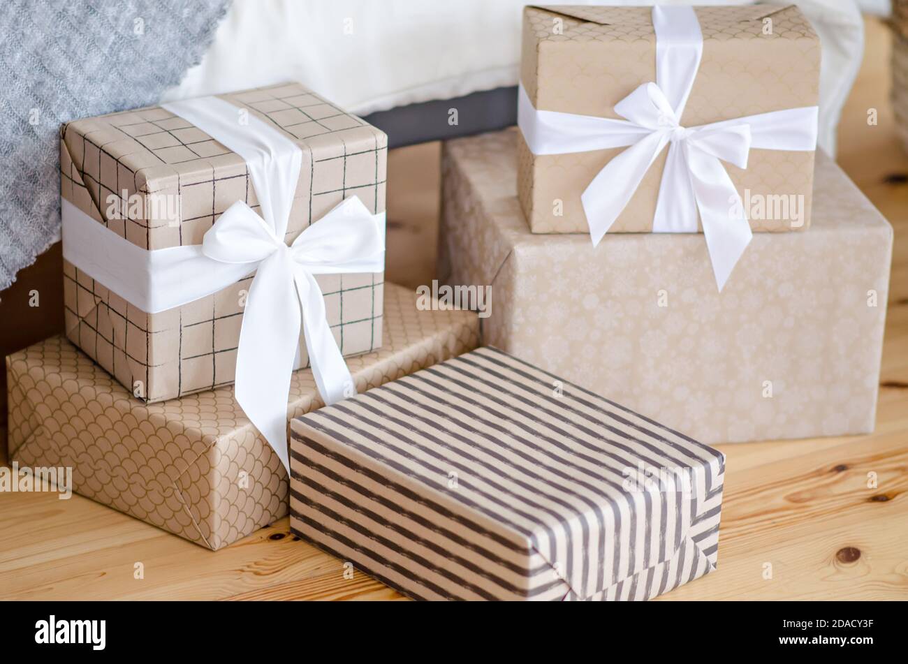Auf dem Holzboden des Weihnachtsmannes stehen viele Geschenke, die in Bastelpapier eingewickelt sind und mit einem weißen Band mit Schleife verziert sind. Neujahrswunder. Weihnachten Stockfoto