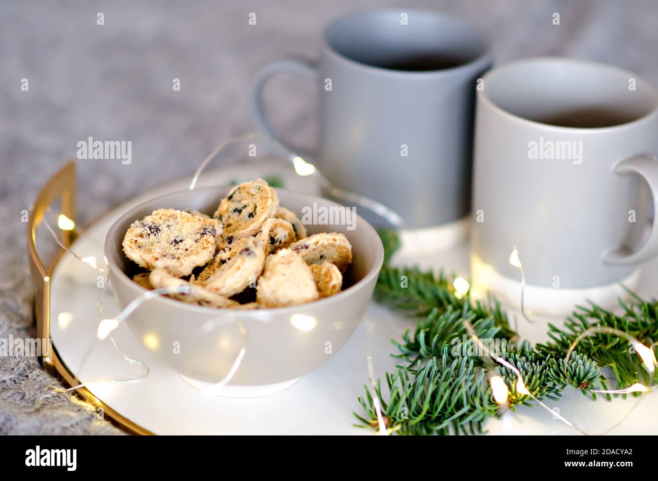 Auf einem Marmortablett mit goldenem Rand befinden sich zwei graue Tassen Tee und ein Schokoladenkekse. Ein Leckerbissen für den Weihnachtsmann. Christbaumzweig Stockfoto