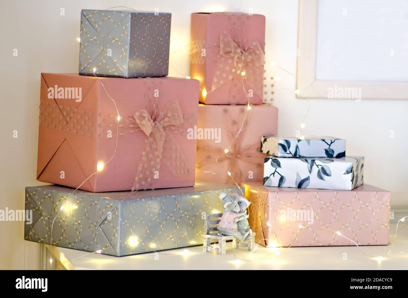 Viele Geschenke in rosa und grauem Papier eingewickelt, mit Luftbändern mit Schleife verziert, Girlanden sind auf dem Tisch von Santa Claus. Neujahrswunder. Stockfoto