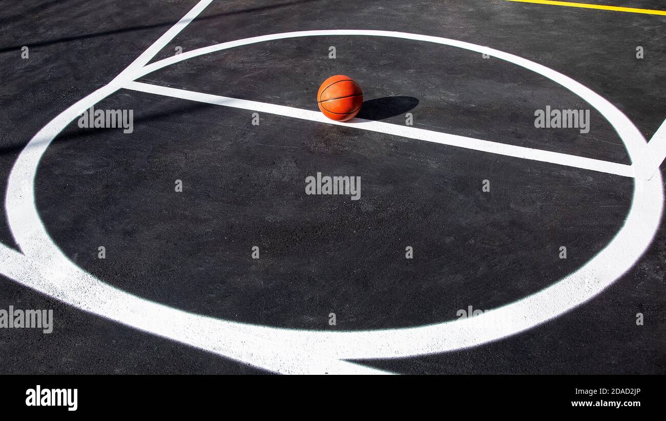 Orange gestreiften Basketball-Ball steht im Kreis auf der Markierung  Spielfeld mit Asphalt Asphalt Asphalt, Sportobjekt durch Sonnenlicht auf  Spielplatz mit Co beleuchtet Stockfotografie - Alamy