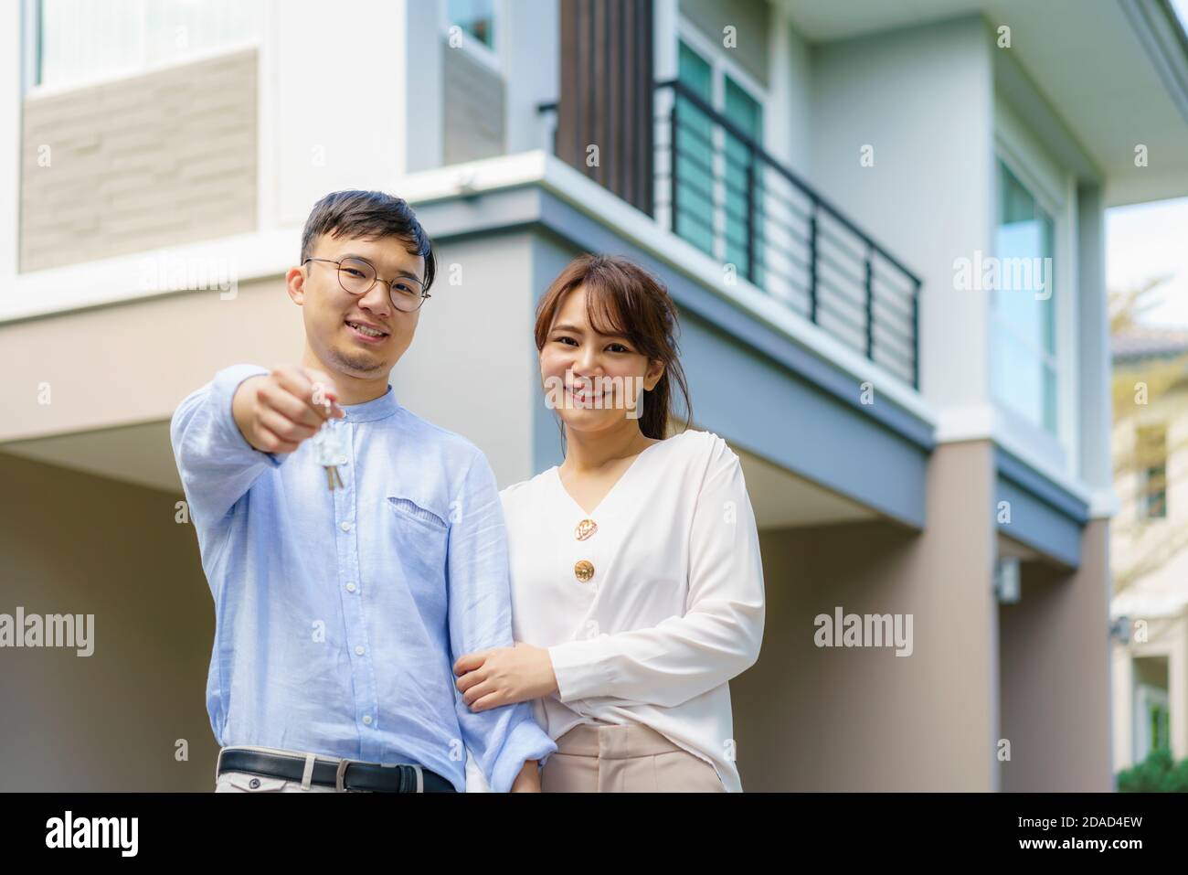 Porträt des jungen asiatischen Paares, das zusammen steht und umarmt und die Haustaste hält, die vor ihrem neuen Haus glücklich aussieht, um neues Leben zu beginnen. Familie Stockfoto
