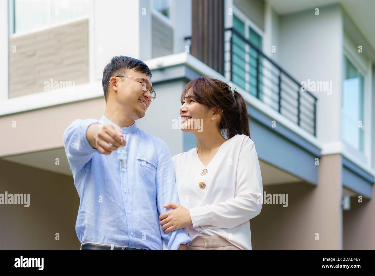 Porträt des jungen asiatischen Paares, das zusammen steht und umarmt und die Haustaste hält, die vor ihrem neuen Haus glücklich aussieht, um neues Leben zu beginnen. Familie Stockfoto