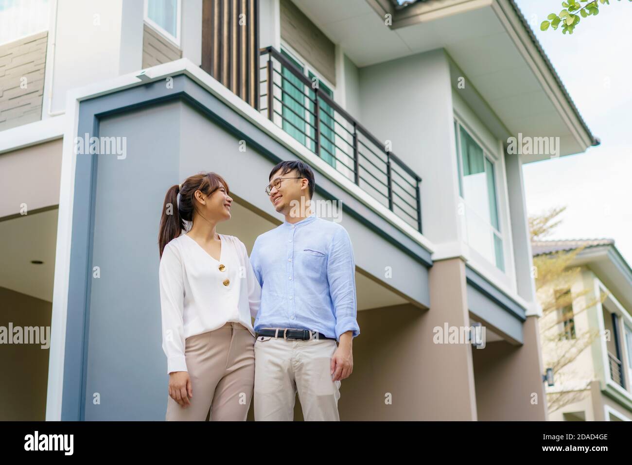 Porträt des jungen asiatischen Paares, das zusammen steht und umarmt und vor ihrem neuen Haus glücklich aussieht, um neues Leben zu beginnen. Familie, Alter, Zuhause, echte Esta Stockfoto