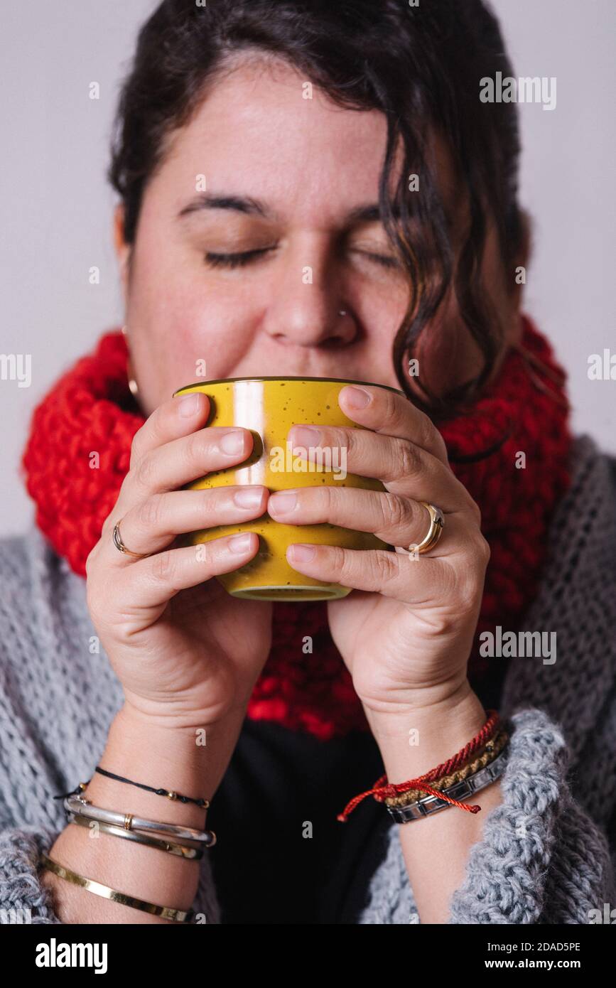 Vertikales Bild einer Frau, die Tee aus einer gelben Tasse trinkt. Sie erwärmt sich mit etwas heißem. Winterkonzept Stockfoto