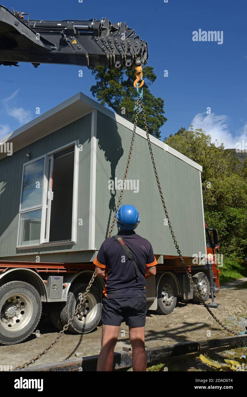 GREYMOUTH, NEUSEELAND, 21. OKTOBER 2020: Ein Kranführer arbeitet daran, ein kleines Gebäude von einem LKW auf seine Pfeiler zu heben. Stockfoto