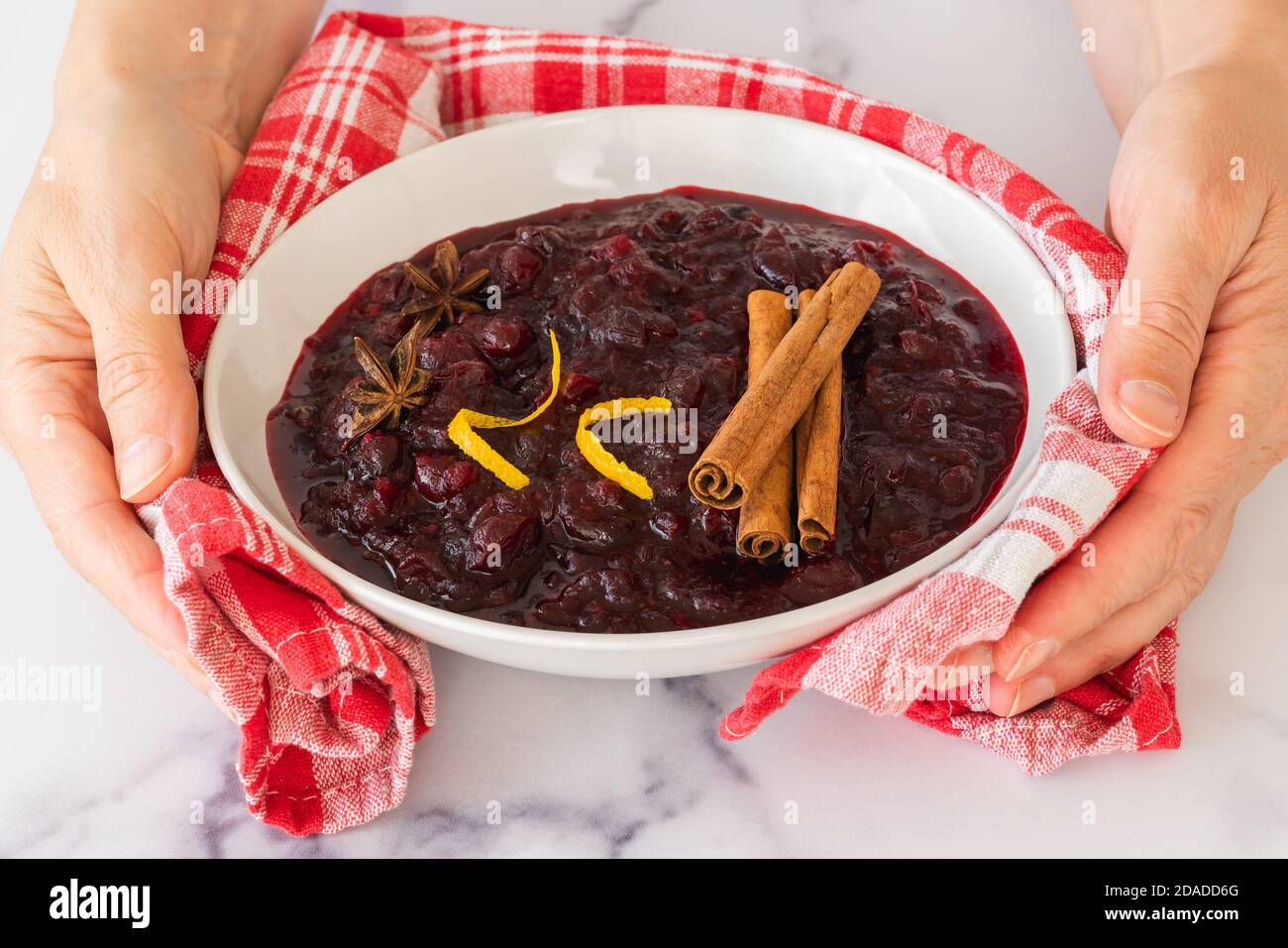 Schüssel mit hausgemachten leckeren Cranberry-Sauce mit Zimt und Anis Stern in einer Schüssel schließen, Frau Hände, hellen Marmor Hintergrund Stockfoto