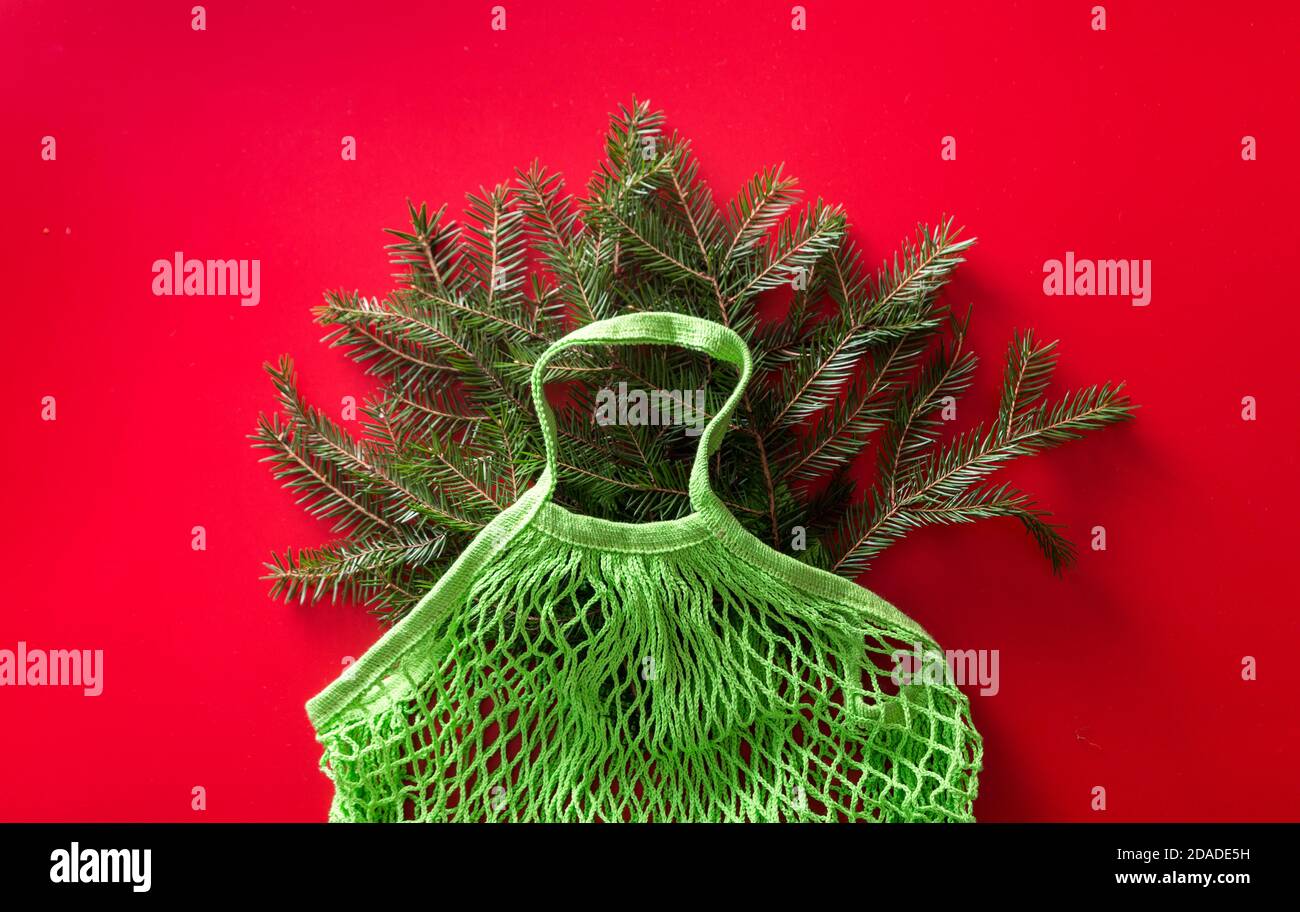 Netztasche aus grüner Baumwolle mit Tannenzweigen und rotem Hintergrund. Keine Verschwendung. Umweltfreundliche Weihnachten. Blick von oben. Stockfoto