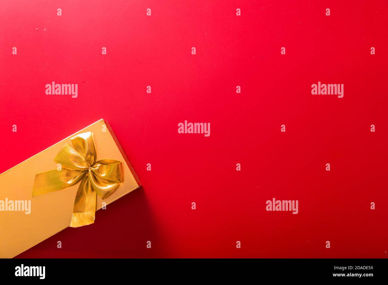 Geschenk in goldener Verpackung mit Schleife auf rotem Hintergrund Stockfoto
