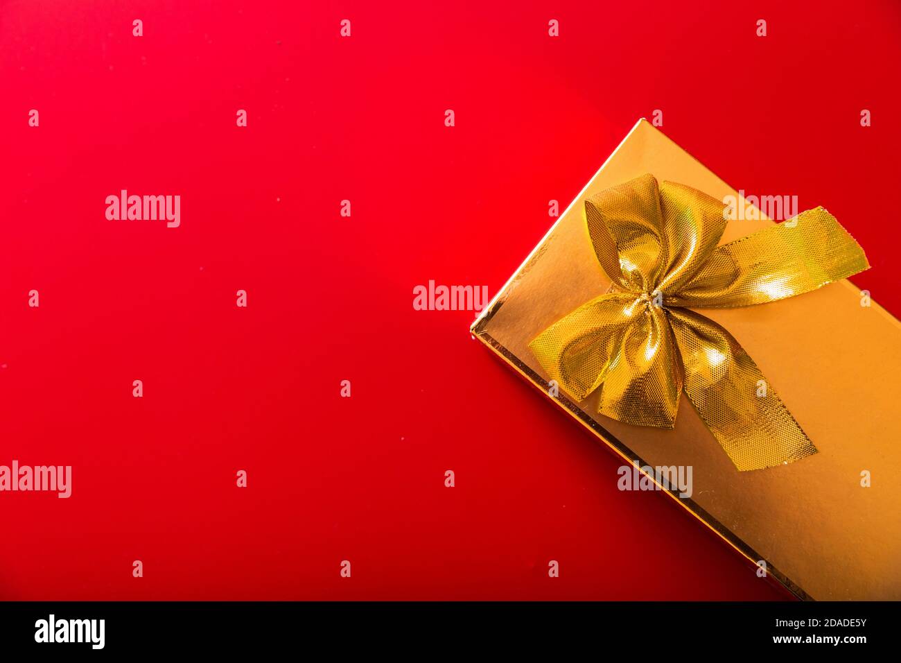 Geschenk in goldener Verpackung mit Schleife auf rotem Hintergrund Stockfoto