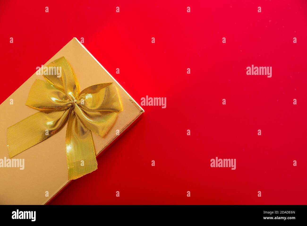 Geschenk in goldener Verpackung mit Schleife auf rotem Hintergrund Stockfoto